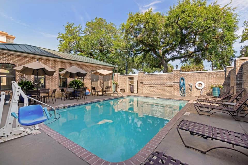 Hotel courtyard pool surrounded by brick building, umbrellas, lounge chairs, and trees