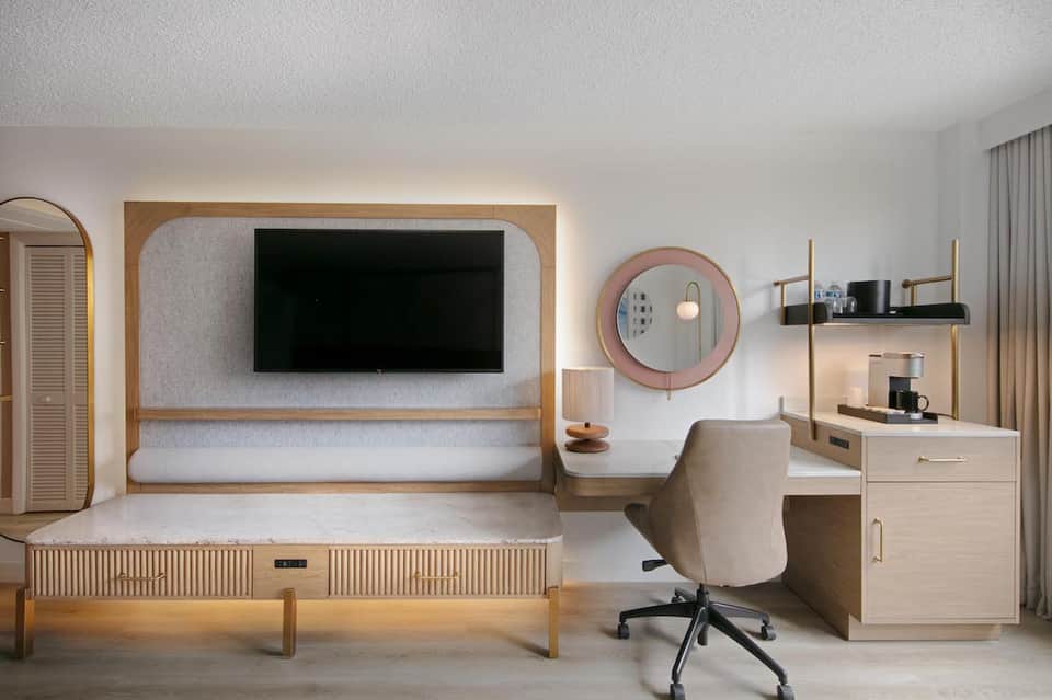 Modern hotel room with wooden bed frame, TV with surround, desk chair, and contemporary furnishings