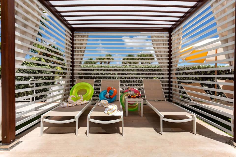 Covered terrace with horizontal louvers, lounge chairs, toys, and ocean view through screens