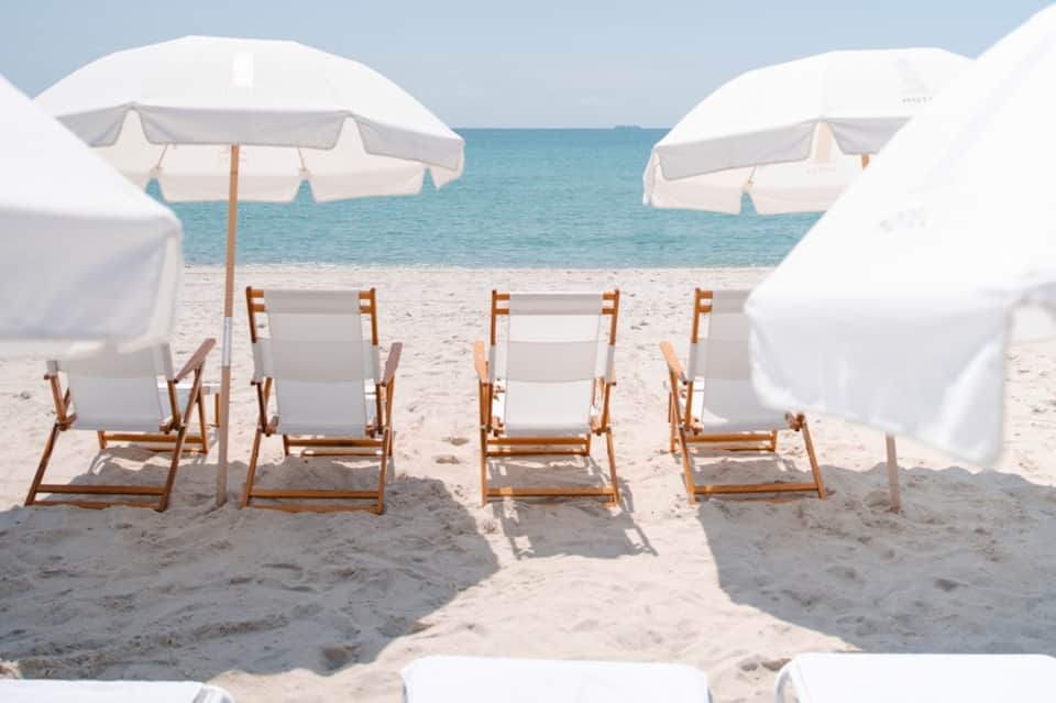 Beach cabanas with white umbrellas and wooden loungers facing turquoise ocean