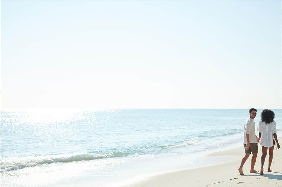 Couple walking on pristine white sandy beach with turquoise waves in background