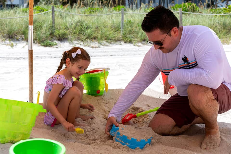 Father and daughter playing with toys in sand at beach with colorful buckets