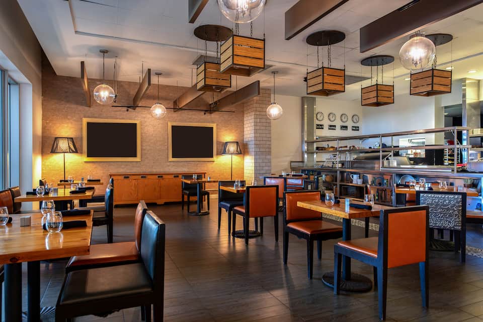 Contemporary restaurant dining area with orange chairs, brick walls, and open kitchen
