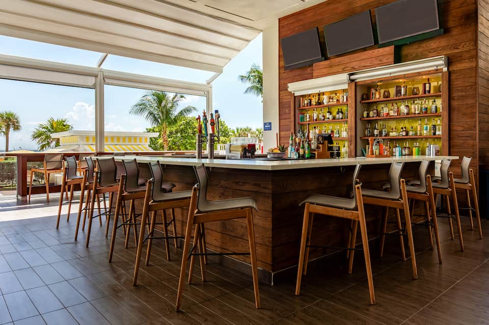 Contemporary resort bar with wooden counter, full liquor shelves, and ocean views