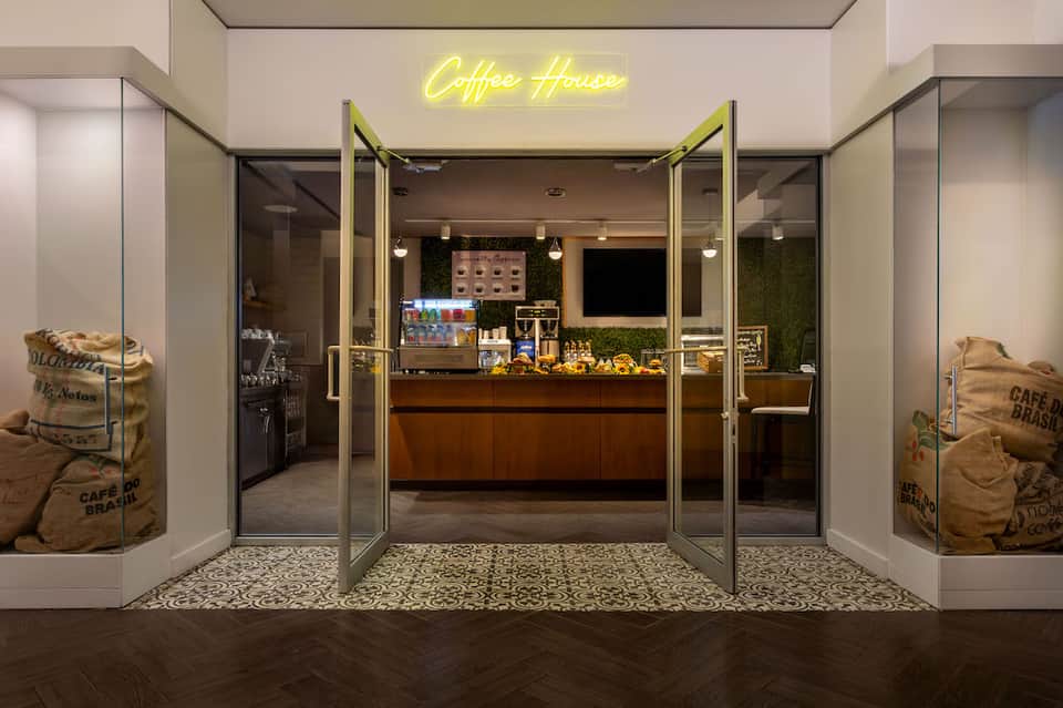 Coffee house entrance with neon sign, glass doors, wooden counter, and decorative coffee bean displays