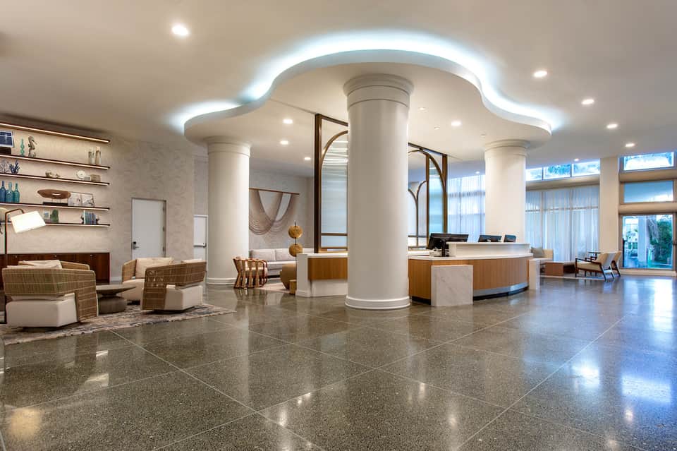 Modern hotel lobby with polished terrazzo floors, white columns, curved ceiling with LED lighting, and wooden reception desk