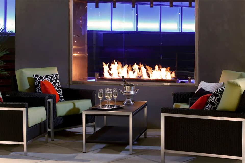 Modern fireplace lounge with black and green seating, decorative pillows, and floor-to-ceiling windows at dusk