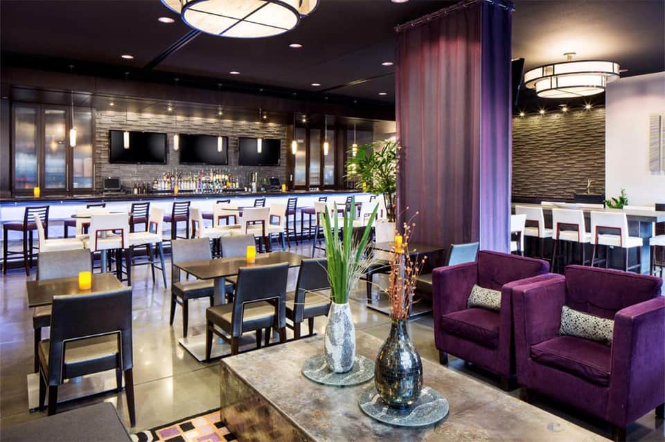 Contemporary hotel bar and lounge with purple seating, marble countertop, and ambient lighting