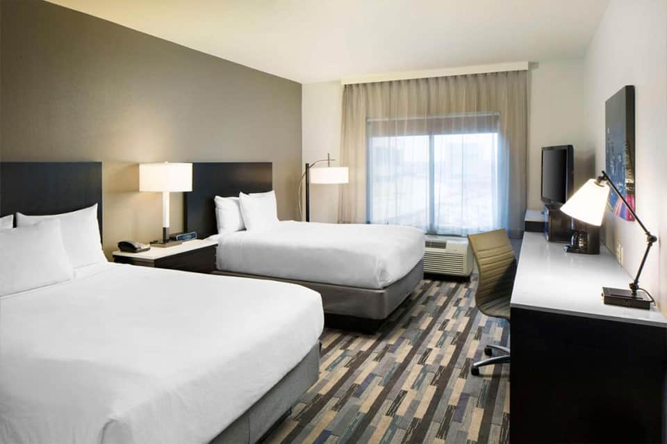 Modern hotel room with two queen beds, flat-screen TV, and glass patio doors