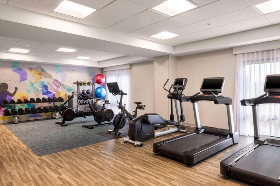Bright fitness facility with treadmills, stationary bikes, dumbbells, and colorful motivational wall mural