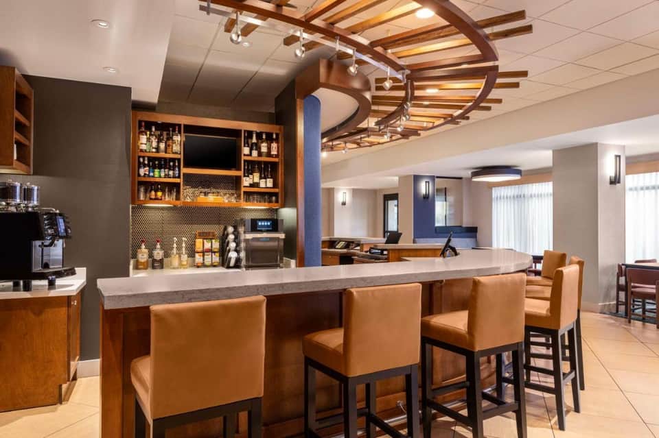 Modern hotel bar with wooden ceiling beams, leather seating, and well-stocked liquor shelves