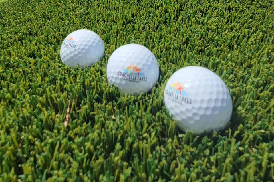 Three white golf balls with orange palm logo on green grass fairway
