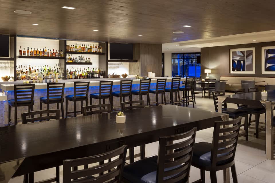 Modern hotel bar and lounge with black chairs, blue cushions, and extensive liquor selection