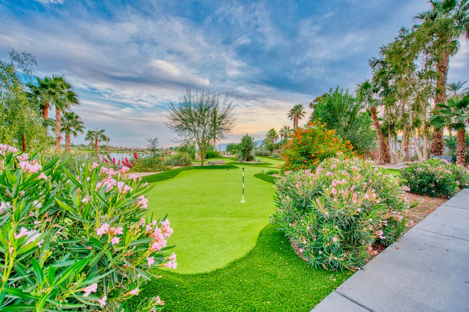 Lush green golf course with colorful flower beds, palm trees, and distant mountains