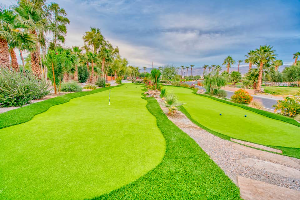 Mini golf course with bright green fairways, palm trees, and desert mountains in background