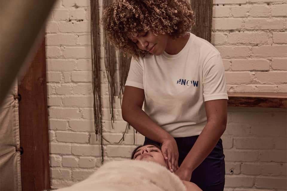 Spa therapist performing massage treatment on client wearing NOW branded shirt