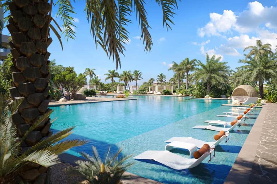 Resort pool with turquoise water, palm trees, loungers, and sunny skies