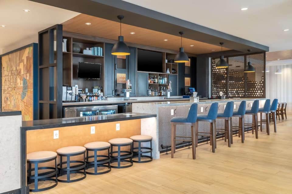 Contemporary hotel bar with blue seating, wood accents, pendant lighting, and dark cabinetry