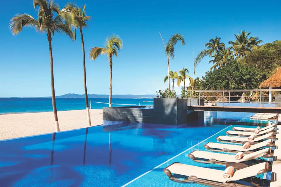 Luxury resort infinity pool overlooking tropical beach with palm trees and ocean view