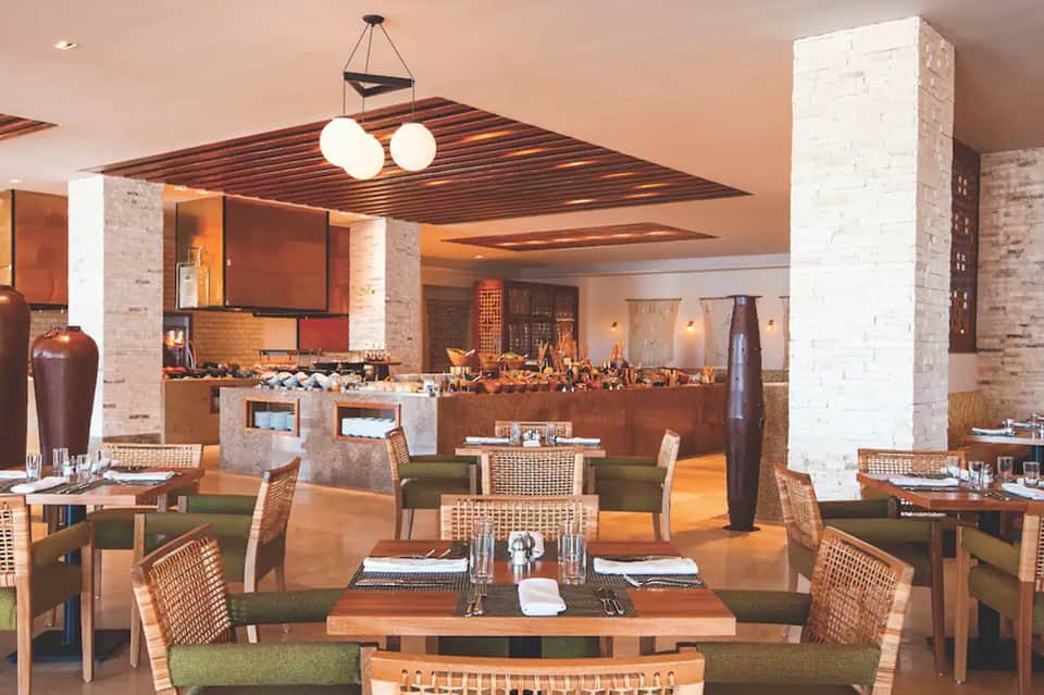 Upscale dining room with brick columns, woven chairs, warm lighting, and modern bar area