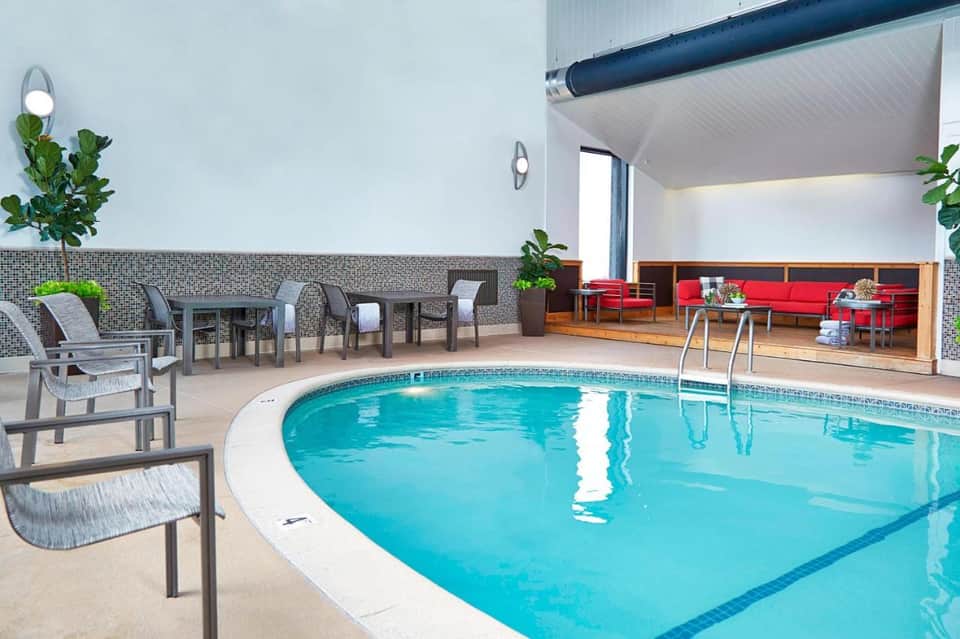 Indoor lap pool with turquoise water, lounge chairs, and seating area with red sofa visible