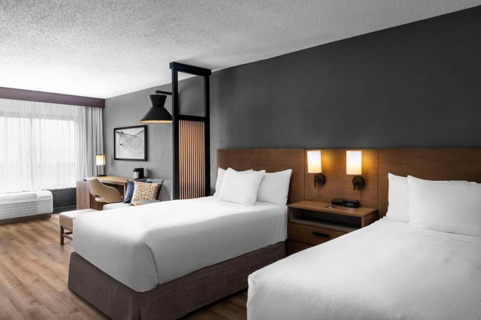 Contemporary hotel bedroom with two queen beds, dark accent wall, and modern lighting