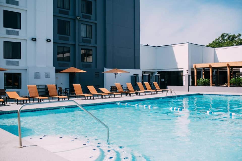 Modern resort pool with orange lounge chairs, umbrellas, and contemporary building architecture