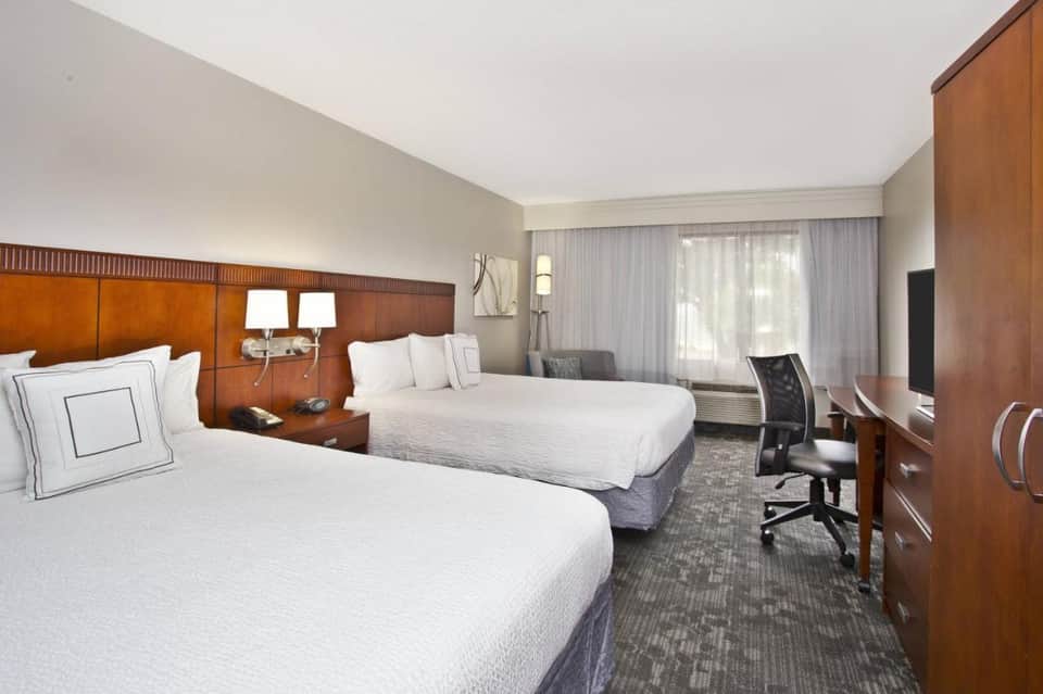 Hotel guest room with two queen beds, wood headboard, desk area, and modern furnishings