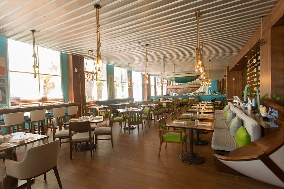 Modern restaurant dining area with wood furnishings, pendant lighting, and large windows