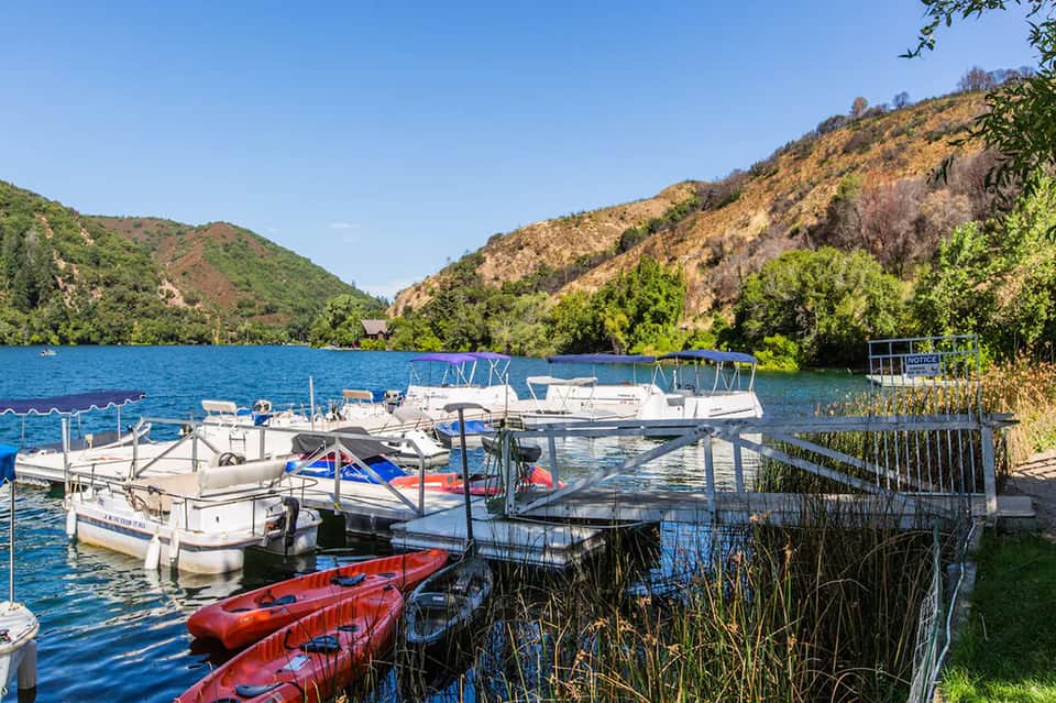 Scenic mountain lake with docked boats, kayaks, forested hills, and autumn foliage