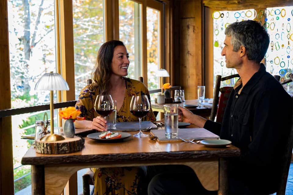 Couple dining at restaurant table with forest view and wine glasses