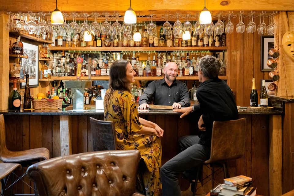 Upscale wooden bar with bartender serving guests, extensive bottle collection