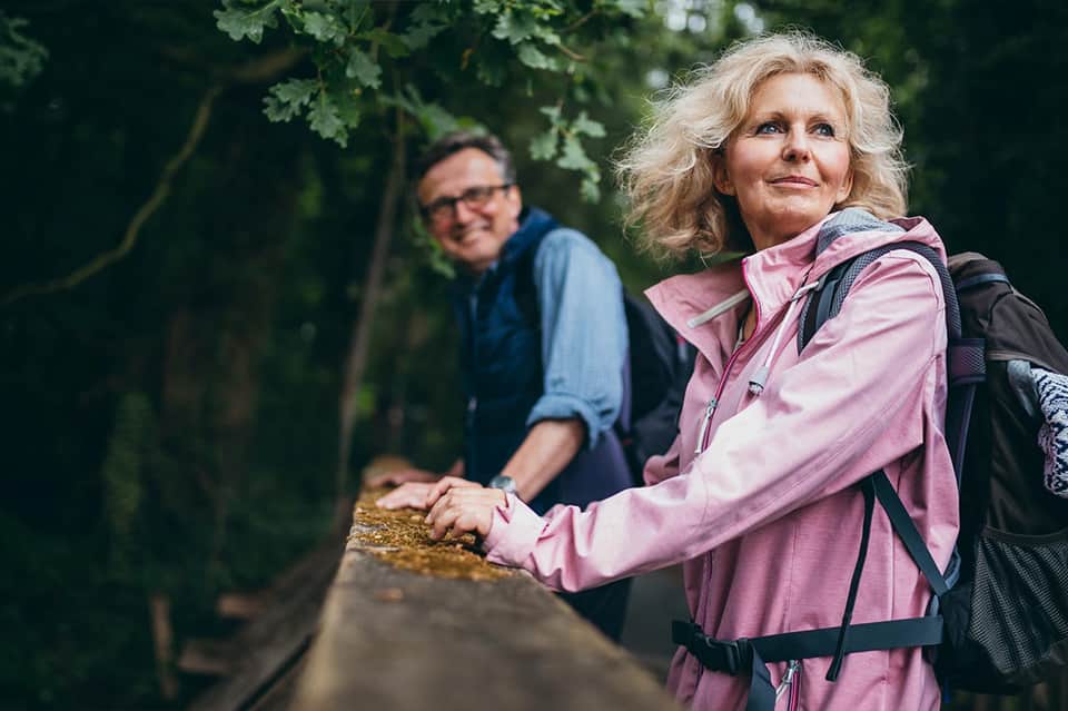 Older couple hiking on woodland trail, woman in pink jacket