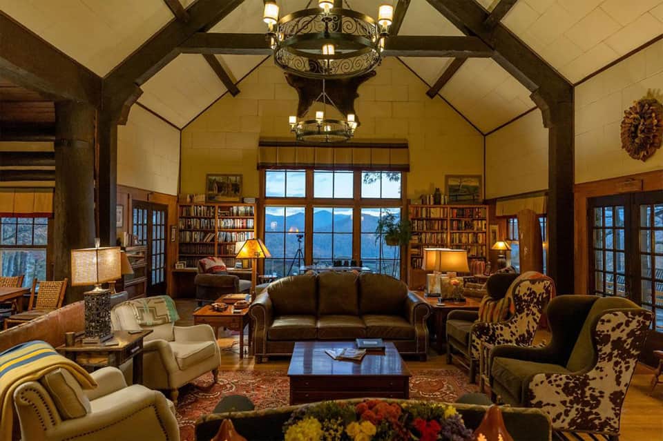 Spacious lodge interior with exposed wooden beams, fireplace, bookshelves, and panoramic ocean views