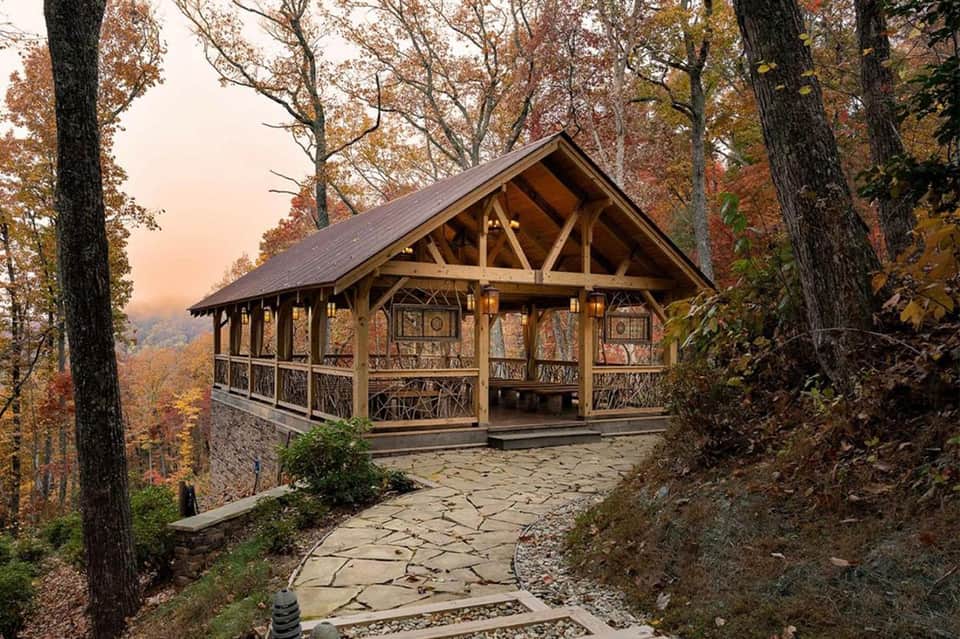 Rustic wooden pavilion with stone patio nestled among autumn trees on hillside at dusk