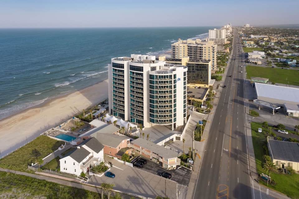 Aerial view of beachfront resort building with sandy beach, ocean, and coastal landscape