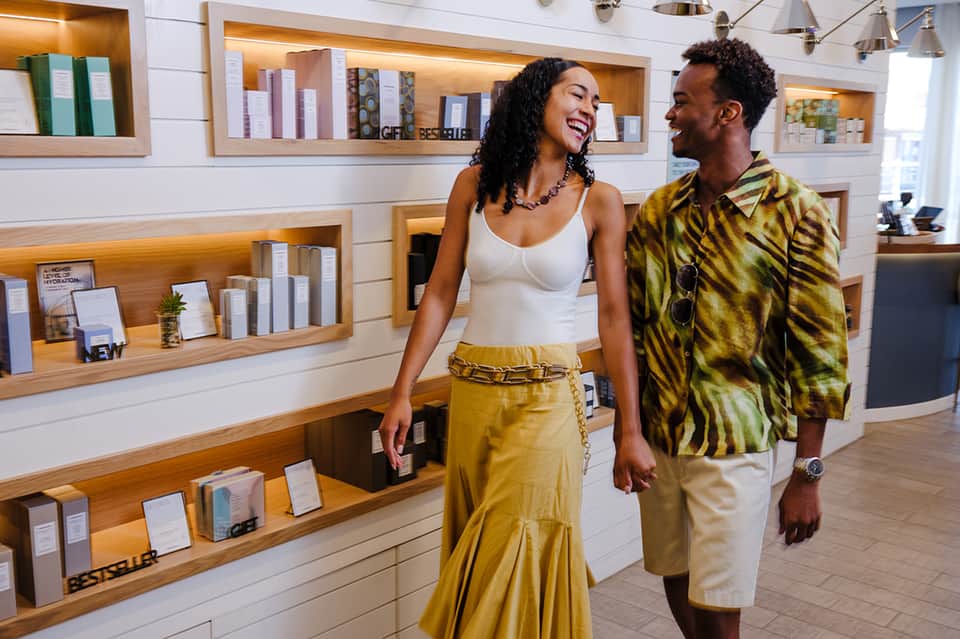 Hotel lobby with two guests browsing products displayed on wooden shelves with warm accent lighting