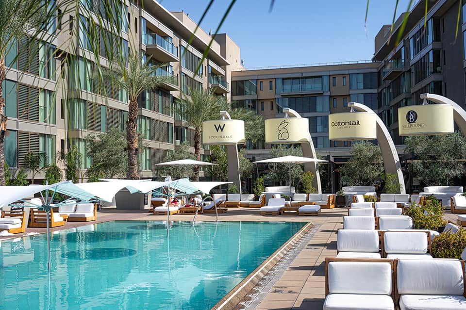 Outdoor resort pool with turquoise water, white lounge chairs, branded umbrellas, and modern residential buildings