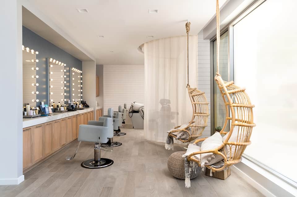 Spa beauty salon with vanity mirrors, bright lighting, hanging wicker chairs, and modern aesthetic