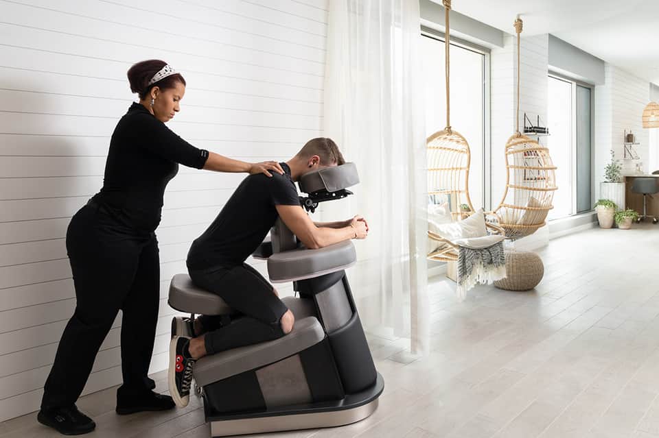 Spa treatment room with massage chair and therapist performing neck massage near hanging wicker chairs