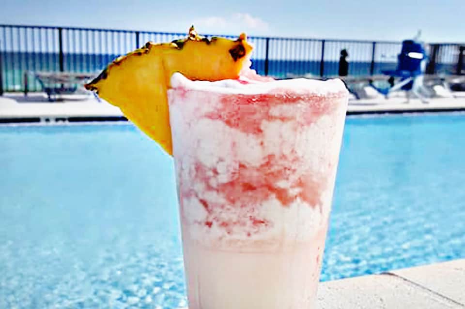 Tropical cocktail with pineapple garnish by resort pool under blue sky