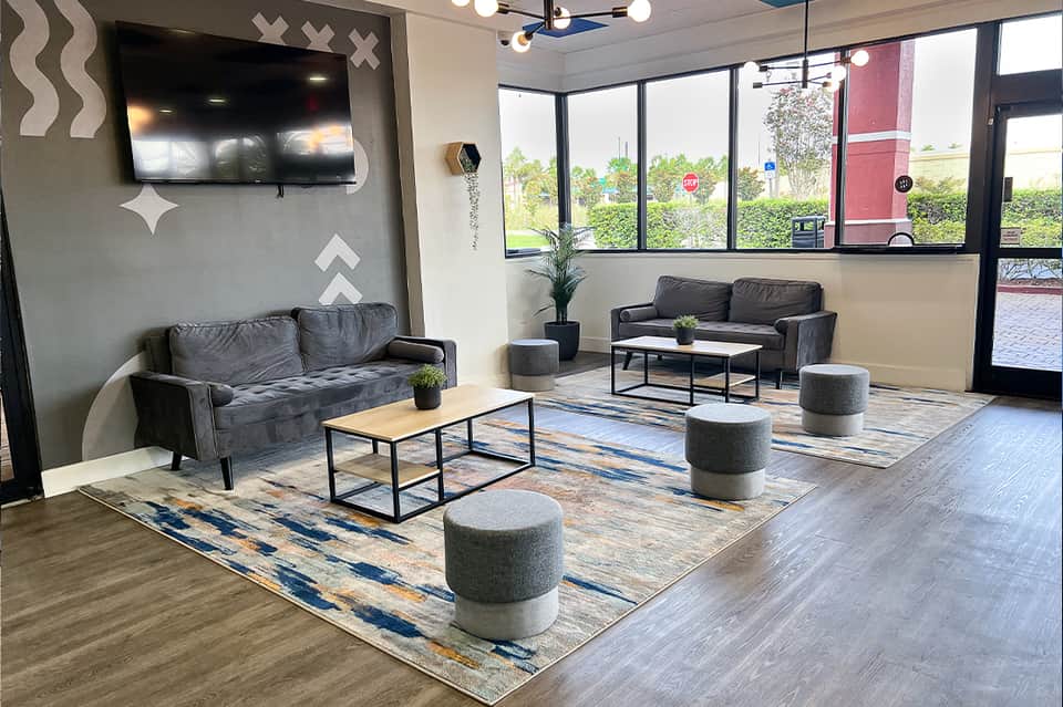 Contemporary hotel lobby lounge with gray sofas, geometric wall art, modern furniture, and large windows