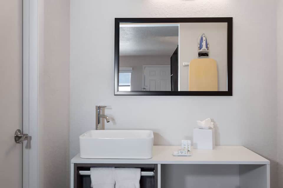 Clean bathroom vanity with white rectangular sink, black-framed mirror, and hotel amenities