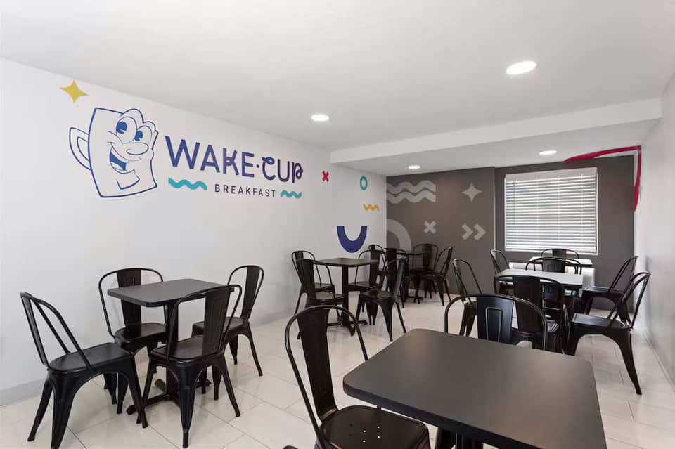 Casual breakfast cafe with cheerful Wake Cup logo, black metal tables and chairs, and geometric wall art
