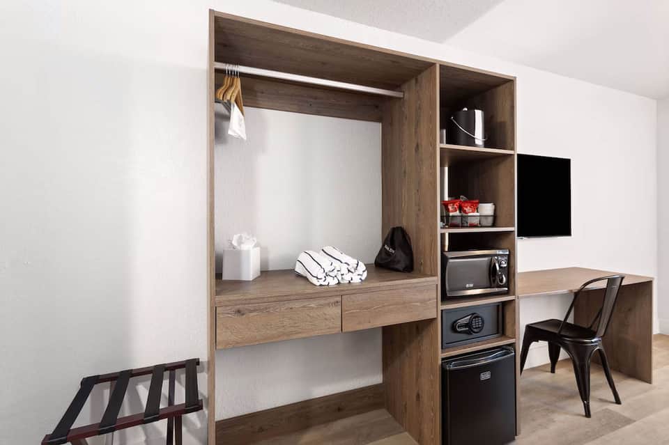 Modern hotel room wardrobe with desk, shelving, TV, and wooden cabinetry