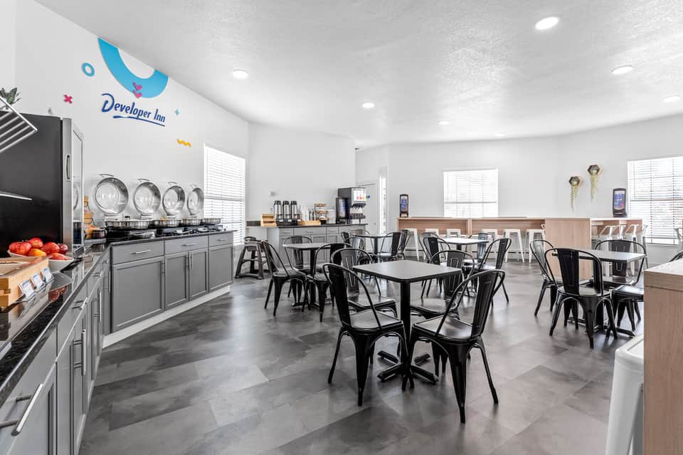 Developer Inn breakfast area with bright white walls, modern kitchen counter, dining tables, and colorful logo wall art