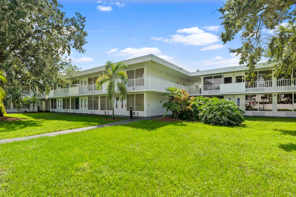 Two-story resort building with white railings, palm trees, and manicured green lawn