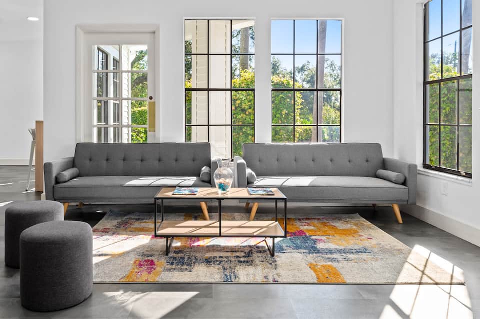 Modern living room with gray sofas, large windows overlooking green landscape, and colorful geometric rug
