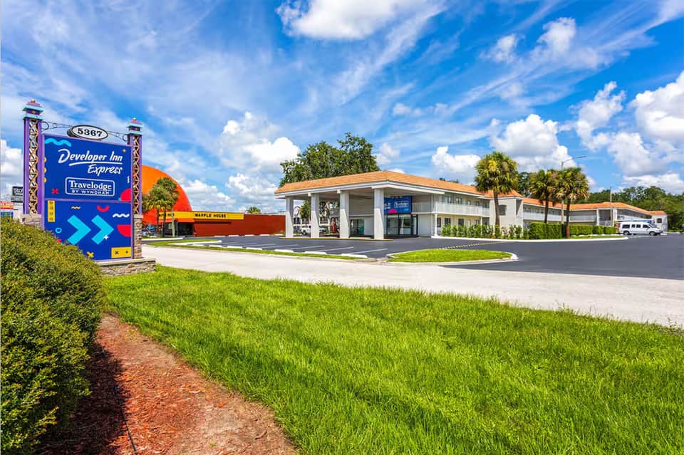 Retro-style Developer Inn Express motel exterior with colorful signage, palm trees, and parked vehicles