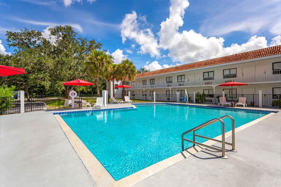 Resort pool with turquoise water, red umbrellas, and palm trees with tropical landscaping